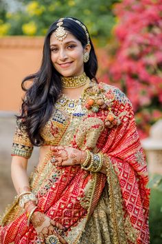 a woman in a red and gold bridal outfit posing for the camera with her hands on her hips