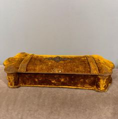 an old yellow velvet covered bench on the floor