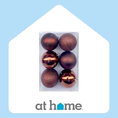 six shiny brown ornaments in a package with the at home logo on top of it