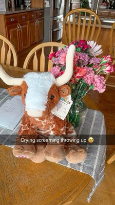 a stuffed cow sitting on top of a table next to a vase filled with flowers