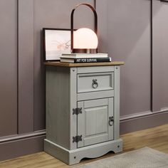 a nightstand with a lamp on top of it next to a purple wall and wooden floor