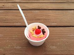 an ice cream sundae with cherries and cereals in a plastic cup on a wooden table