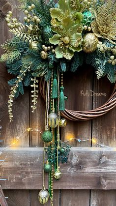 a wreath with green and gold decorations hanging on a wooden wall next to a fence