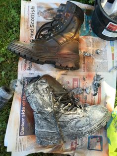 two pairs of dirty shoes sitting on top of newspaper next to a helmet and water bottle