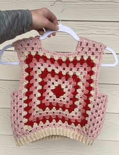 someone is holding up a crocheted pink and red sweater on a hanger