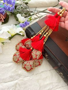 a pair of red tassels hanging from a book with flowers in the background