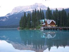 a lake surrounded by trees with a house on the dock and mountains in the background