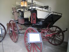 an old fashioned horse drawn carriage on display in a museum setting with red wheels and spokes