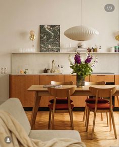 a dining room table and chairs in front of an open kitchen area with white walls