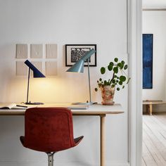 a desk with a lamp, potted plant and pictures on the wall