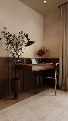 a room with a desk, chair and potted plant on it in front of a window