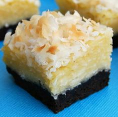 three pieces of cake with coconut toppings on a blue tablecloth and one piece is cut in half