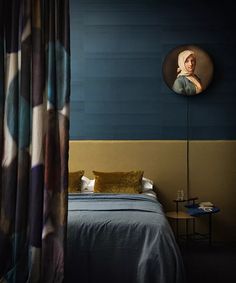 a bedroom with blue walls and a painting hanging on the wall above it's bed