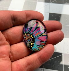 a hand holding a colorful glass cabochon in it's left hand on a checkered tile floor