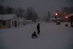 two people are standing in the snow on a sled pulled by a small child