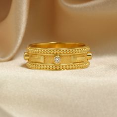 a gold ring with two rows of beads and a single diamond on the middle, sitting on a white cloth