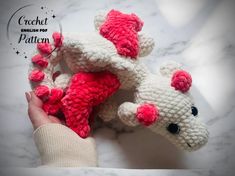 a hand holding two crocheted stuffed animals on top of a marble countertop