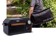 a man holding a black bag next to a small machine in front of some trees