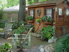 a small wooden shed with flowers in the window boxes on the side and chairs around it