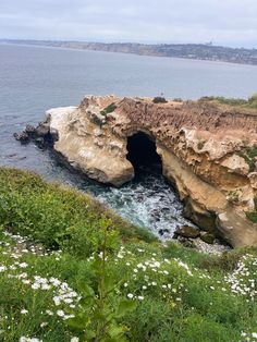 a large rock formation near the ocean with water coming out of it's entrance