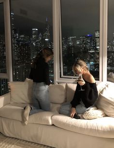 two women sitting on a couch looking at their cell phones in front of the city lights