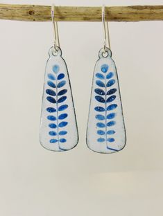 two blue and white leaf shaped earrings hanging from a wooden hook on a twig