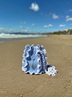 a blue crocheted purse sitting on top of a sandy beach next to the ocean