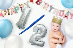 a baby wearing a crown sits in front of balloons and streamers that spell out the number two