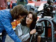 a man and woman looking at an old movie camera on a tripod in the street