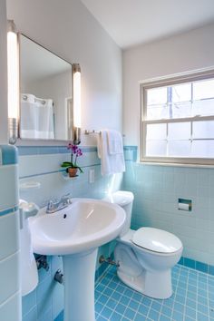 a white toilet sitting next to a sink in a bathroom under a window with blue tiles on the floor