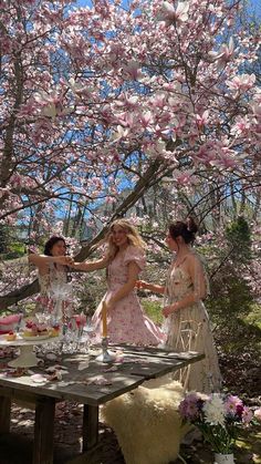 three women standing around a table in front of a tree with pink flowers on it