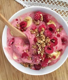 a bowl filled with ice cream topped with raspberries and granola next to a wooden spoon