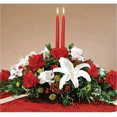 a centerpiece with red roses, white lilies and greenery in front of two lit candles