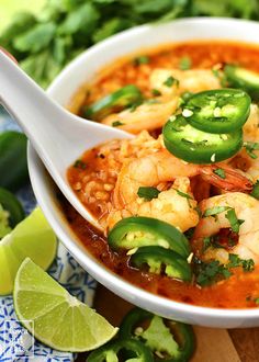 a close up of a bowl of soup with shrimp and jalapenos on the side