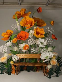 an arrangement of flowers on display in front of a wooden bench with white and orange flowers