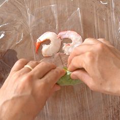 a person holding a piece of lettuce and shrimp in plastic wrap on top of a wooden table