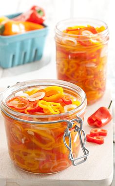 two jars filled with sliced peppers sitting on top of a table next to each other