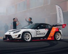 two men standing next to a race car