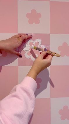 a woman is painting the wall with pink and white flowers on it, while another person holds a paintbrush in their hand