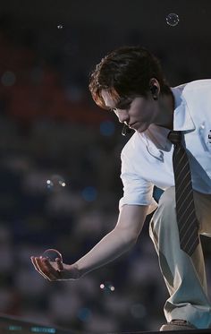 a man in white shirt and tie blowing bubbles on the ground with his hands out