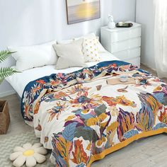 a bedroom with a bed covered in a colorful comforter next to a plant on the floor