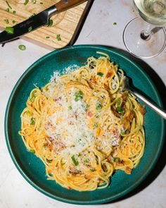 a plate of pasta with parmesan cheese and green peppers on it next to a glass of wine