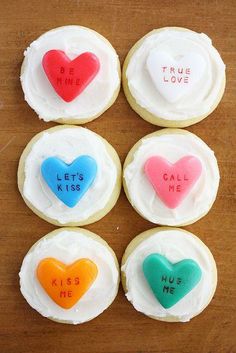 four cookies with conversation hearts on them sitting on a wooden table next to the words true love and let's kiss me