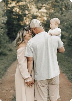 a man and woman holding a baby while standing on a dirt road in the woods