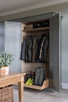 an open closet with clothes and shoes on the shelves, next to a wooden table