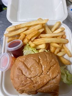 a sandwich and french fries are in a takeout container with ketchup on the side