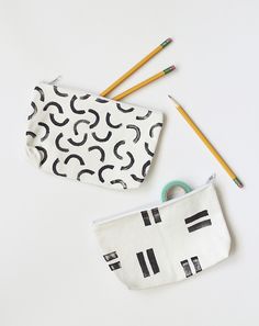 two pencils are sitting next to a zippered pouch with black and white designs