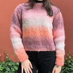 a woman standing in front of a wall wearing a pink and orange sweater