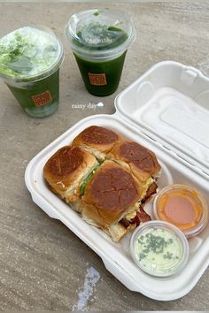 there is a sandwich and two drinks in the trays on the table next to each other