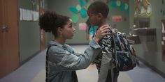 two children are standing in a hallway with backpacks on their shoulders and looking at each other